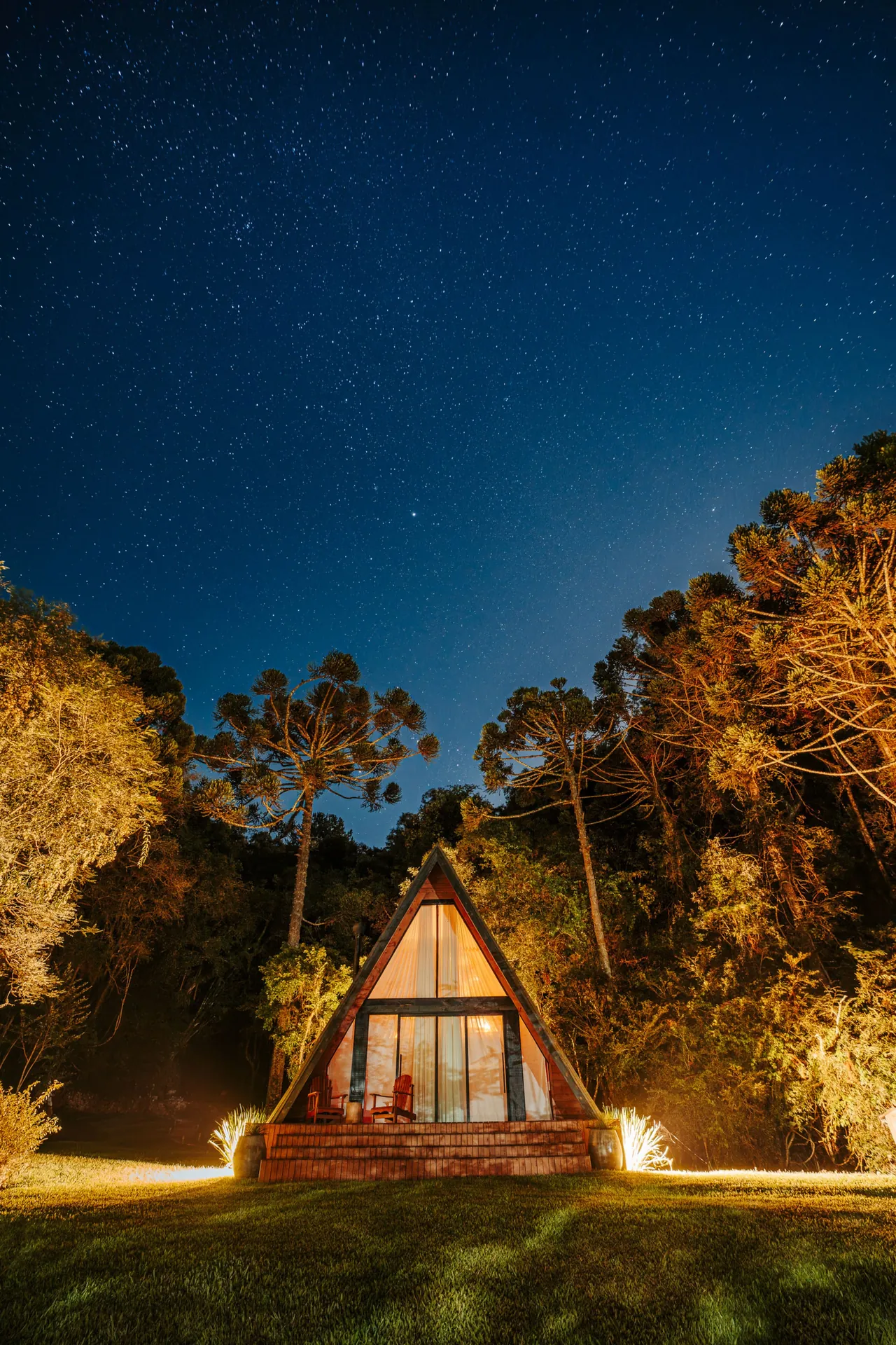 A cabana A-frame iluminada à noite, sob o céu estrelado