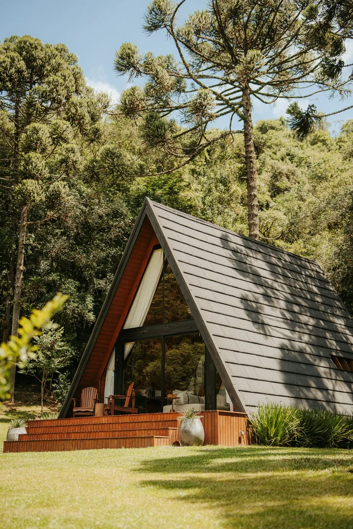 A cabana A-frame no gramado, entre araucárias e mata